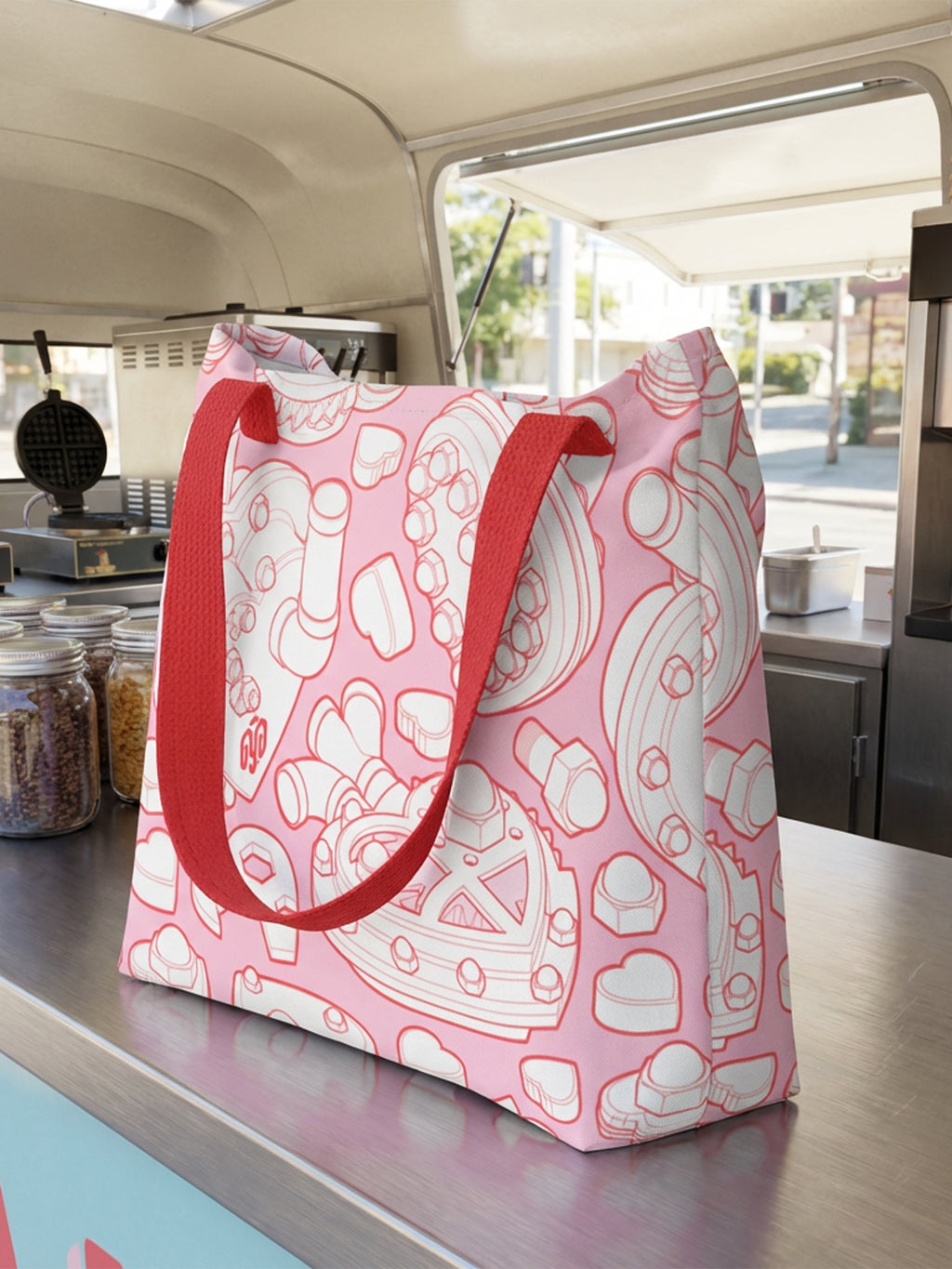 Bolsa tote bag colección “Mecanismos Afectivos” con patrón de corazones mecánicos isométricos, en mostrador de camión de helados.