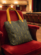 Maqueta de bolsa tote bag en tonos elegantes con patrón de bombillas, en sala de conciertos; diseño de GyGinfographics.