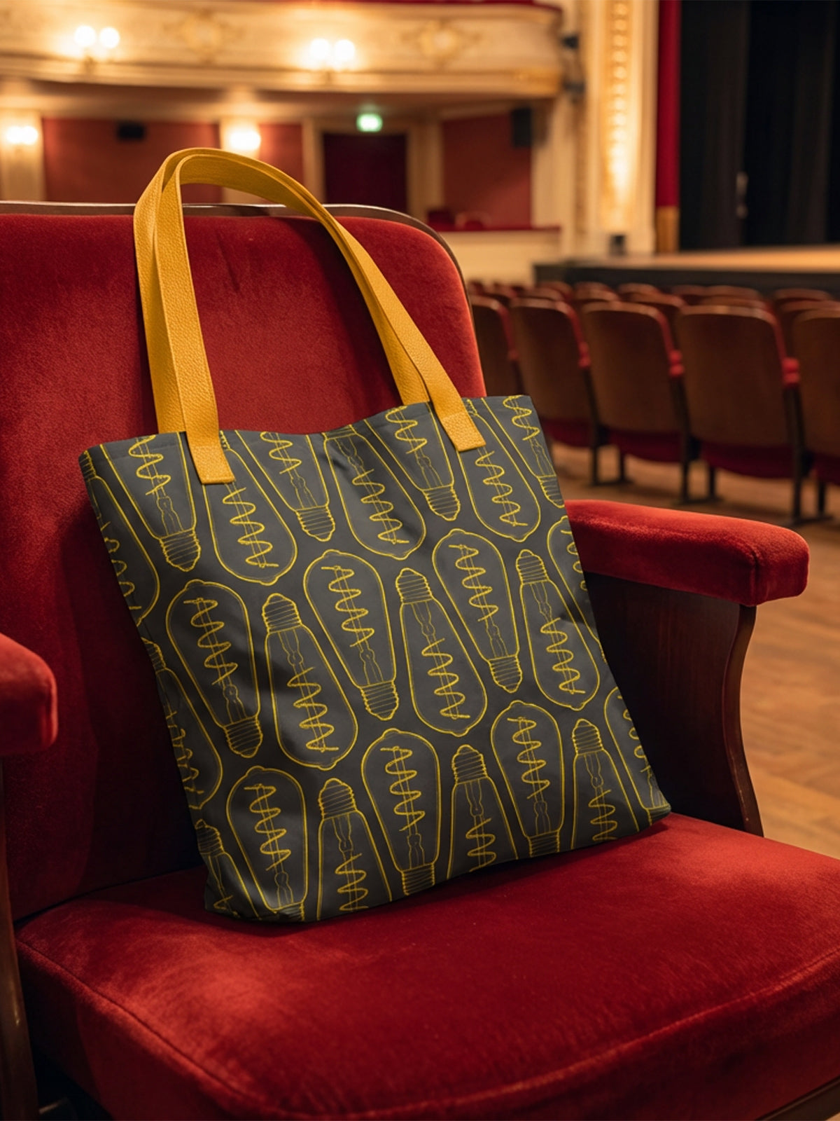Maqueta de bolsa tote bag en tonos elegantes con patrón de bombillas, en sala de conciertos; diseño de GyGinfographics.