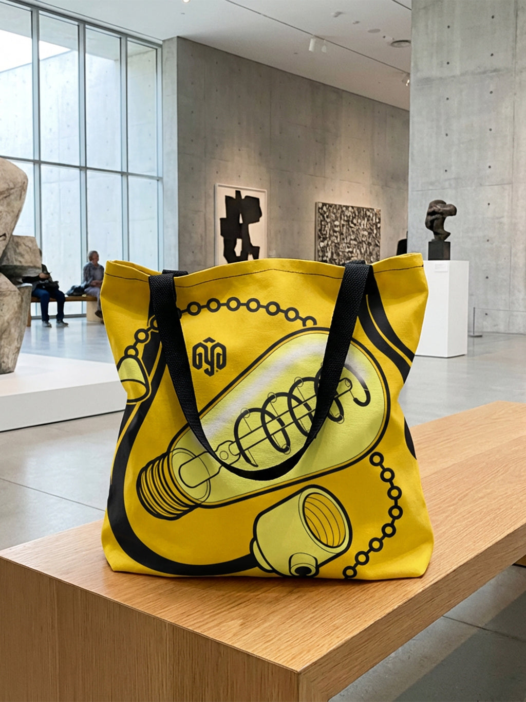 Maqueta de bolsa tote bag en tonos amarillos en museo de arte contemporáneo, con bombilla isométrica diseñada por GyGinfographics y asas tridimensionales.