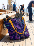 Tote bag con estampado de anclas en tonos morado y azul oscuro sobre la cubierta de un barco de vela.