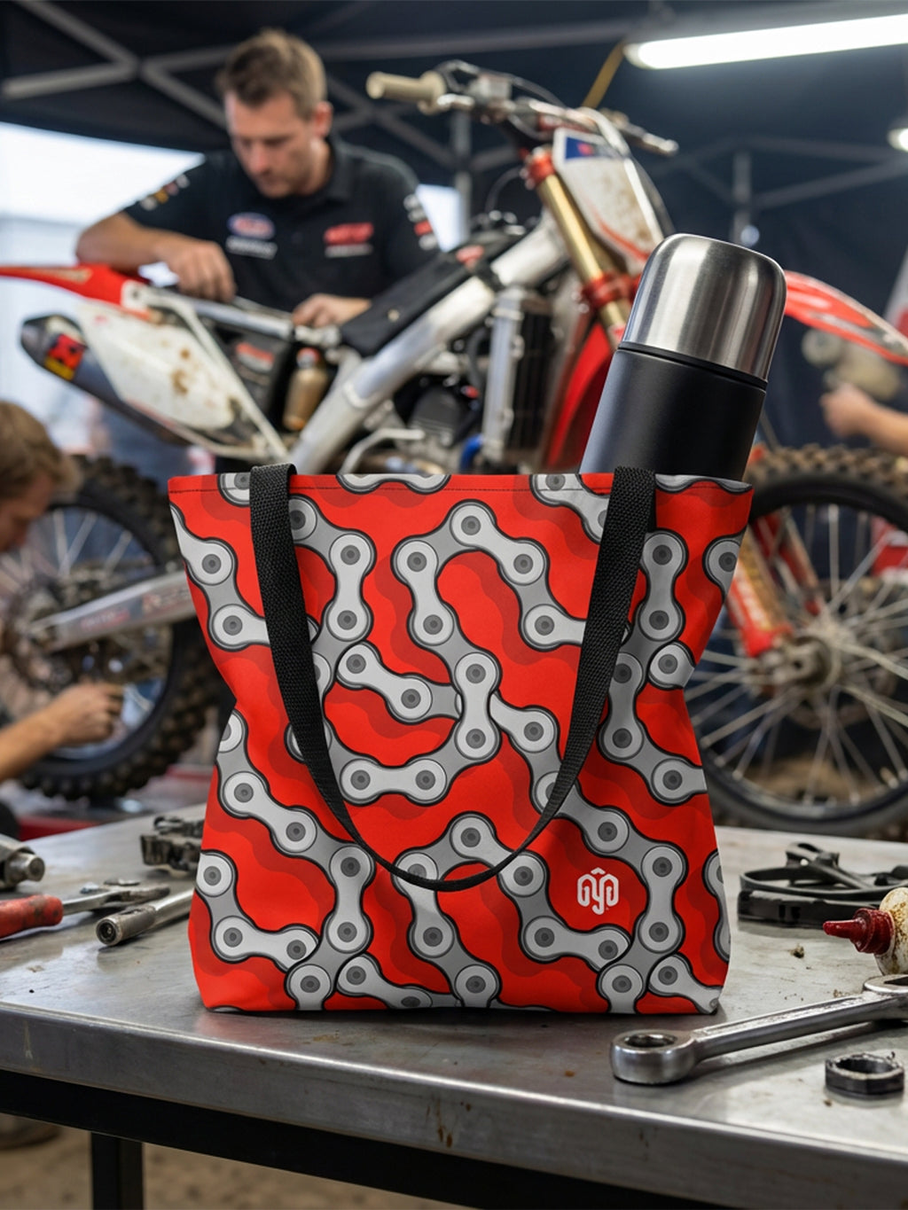 Tote bag with black handles and red and gray bicycle chain print, 3/4 view.