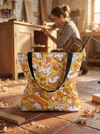 Tote bag con estampado de textura de herramientas de carpintería en tonos amarillos y beige. Al fondo una mujer trabaja un mueble de madera en su taller de carpintería.